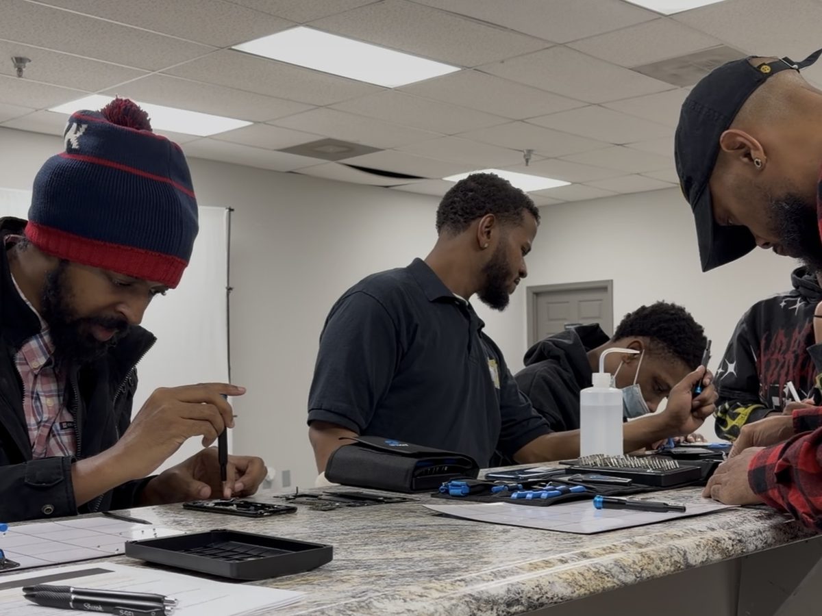 Three students at the counter taking phones apart with iFixit driver kits and parts trays